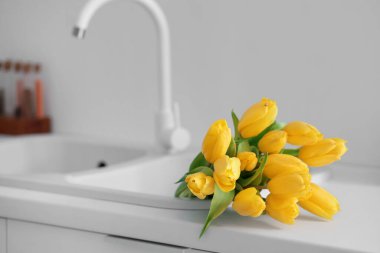 Lavabonun yanındaki beyaz mutfak tezgahında sarı lale çiçekleri.