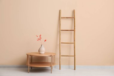 Ahşap merdiven, masa ve vazo. Odadaki bej duvarın yanında lagurus var.