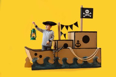 Sarı arka planda karton gemide fenerle oynayan sevimli küçük bir korsan.