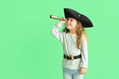 Yeşil arka planda dürbünü olan korsan gibi giyinmiş şirin küçük bir kız.