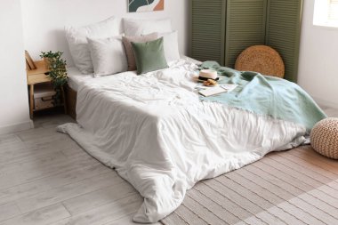 Beyaz battaniyeli rahat yatak, şık bir yatak odasında şapka ve kurabiyeler.