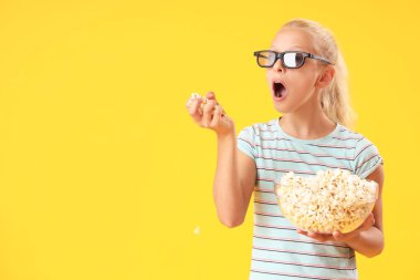 Üç boyutlu sinema gözlüklü tatlı kız sarı arka planda patlamış mısır yiyor.