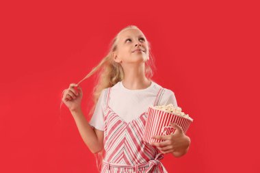 Kırmızı arka planda patlamış mısırı olan düşünceli bir kız.