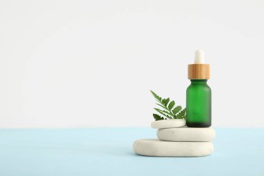 Temel yağ şişesi, yeşil yaprak ve hafif arkaplanda taşlarla kompozisyon
