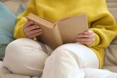 Evdeki kanepede kitap okuyan genç bir kadın, yakın çekim.