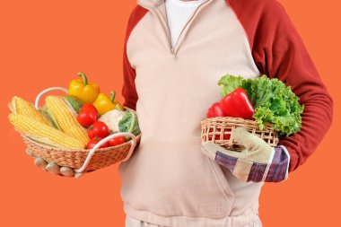 Turuncu arka planda farklı olgun sebzelerle dolu sepetleri olan olgun bir erkek çiftçi.