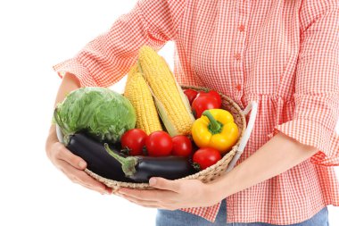 Beyaz arka planda farklı olgun sebzelerle dolu sepeti olan genç bir kadın çiftçi.