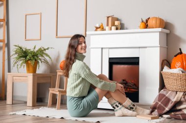 Genç bir kadın şöminenin yanında oturuyor.