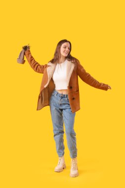 Young woman in winter clothes on yellow background