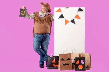 Cadılar Bayramı için giyinmiş olgun bir adam hediye çantası ve pembe arka planda boş bir posterle.