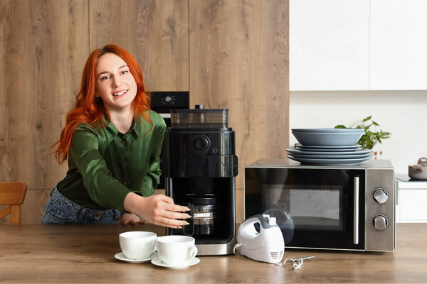 Young redhead woman with coffee machine, microwave oven and mixer in modern kitchen