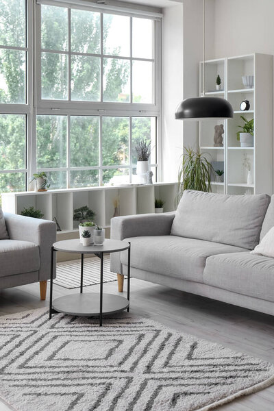 Interior of light living room with cozy grey sofa, coffee table and big window