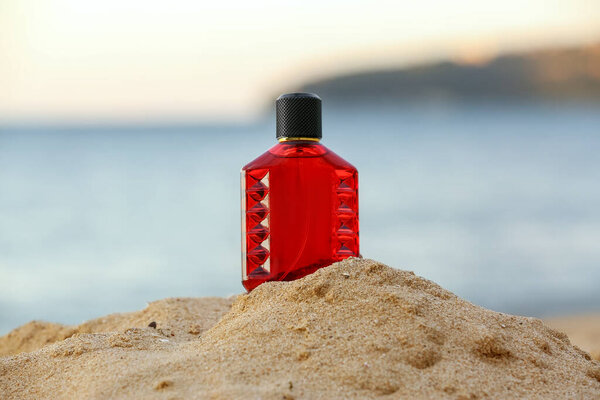 Bottle of luxury perfume on beach sand near ocean