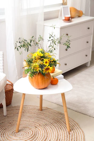Pumpkins with autumn flowers and books on table in living room
