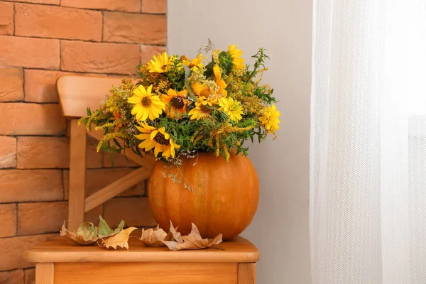 Pumpkin with flowers and fallen leaves on chair in room