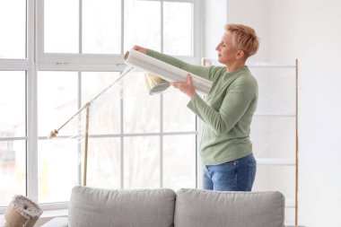 Olgun kadın evinde streç filmle standart lambayı paketliyor.