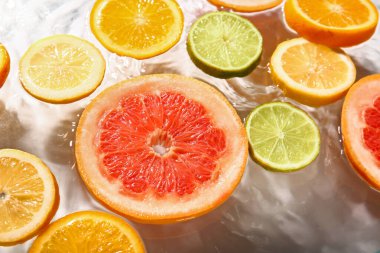 Beyaz arka planda sudaki farklı narenciye dilimleri