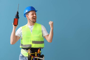 Mavi arka planda matkabı olan mutlu bir erkek inşaatçı.