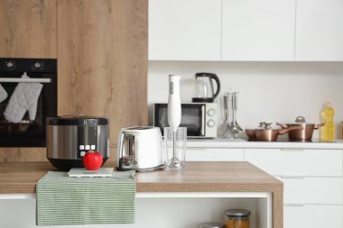 Mutfaktaki ahşap masada blender, tost makinesi, çoklu fırın ve elma.