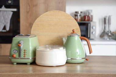 Tost makinesi, elektrikli su ısıtıcı, meyve sıkacağı ve modern mutfakta ahşap masa üzerindeki tahta kesme tahtası.