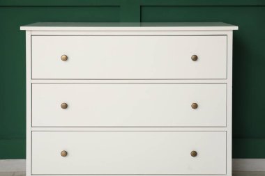 Yeşil duvarın yanında şık beyaz çekmeceler.