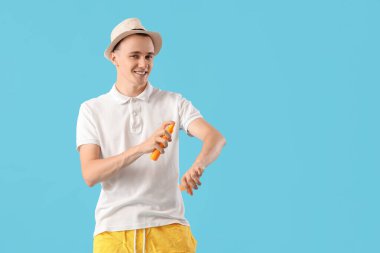 Genç adam mavi arka planda güneş kremi sürüyor.