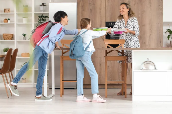 キッチンで彼女の小さな子供たちに学校のランチボックスを与える母 — ストック写真