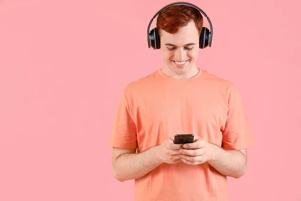 Boldog Fiatal Vörös Hajú Férfi Fülhallgató Mobiltelefon Rózsaszín Háttér — Stock Fotó