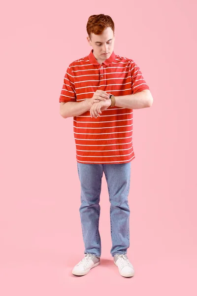 Bedachtzame Jonge Roodharige Man Kijkt Zijn Pols Horloge Tegen Roze — Stockfoto