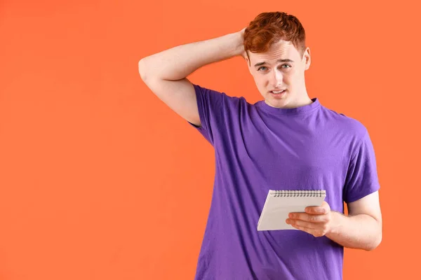Thoughtful young redhead man with notebook on orange background