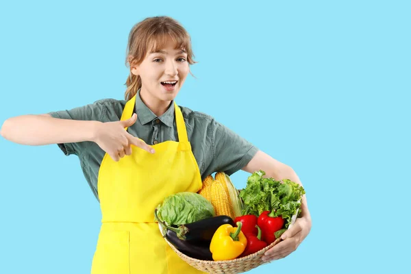 Fröhliche Junge Bäuerin Zeigt Auf Weidenkorb Voller Reifem Gemüse Auf — Stockfoto