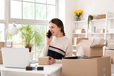 Müşteri için paket taşıyan genç bir kadın ofiste cep telefonuyla konuşuyor.