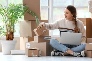 Evde paketli ve dizüstü bilgisayarı olan genç bir kadın.