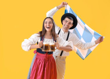 Geleneksel Alman elbiseli genç bir çift bira ve sarı arka planda Bavyera bayrağı