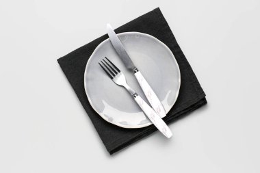 Gri zemin üzerinde çatal bıçak takımı ve peçete olan bir tabak.