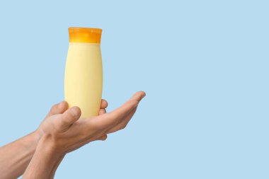 Mavi arka planda güneş kremi şişesi olan kadın elleri.