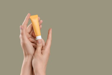 Yeşil arka planda güneş kremi şişesi olan bir kadın el.