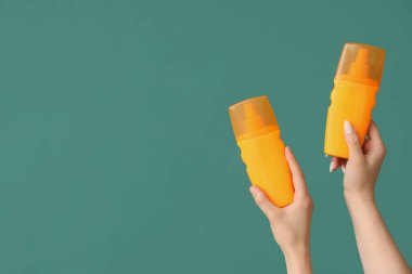 Yeşil arka planda güneş kremi şişeleri olan kadın elleri