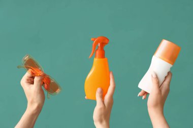 Yeşil arka planda güneş kremi şişeleri ve güneş gözlüğü olan kadın elleri.