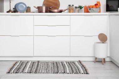 Modern mutfağın içinde şık halı, çöp kutusu ve beyaz tezgahlar var.