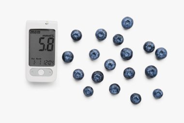 Beyaz arka planda yaban mersinli glukometre. Diyabet kavramı