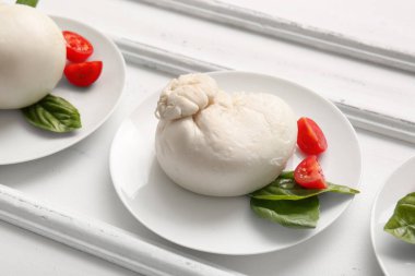 Beyaz arka planda fesleğenli ve domatesli lezzetli Burrata peyniri tabakları.