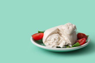 Turkuaz arka planda fesleğenli ve domatesli lezzetli Burrata peyniri.