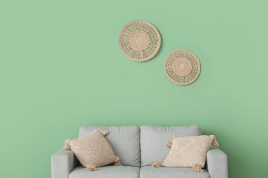 Yeşil duvarın yanında yastıkları olan rahat gri kanepe.