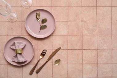 Bej kaplama arka planda altın çatal bıçak takımı olan zarif bir masa.