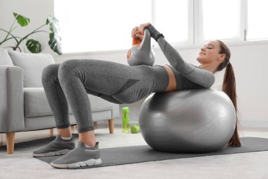 Evde kettlebell ve fitball ile antrenman yapan genç bir bayan.