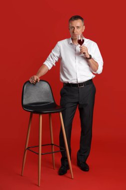 Kırmızı arka planda bir bardak şarap ve dışkısı olan olgun bir adam.