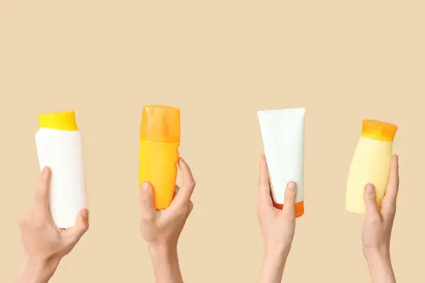Female hands with bottles of sunscreen cream on beige background