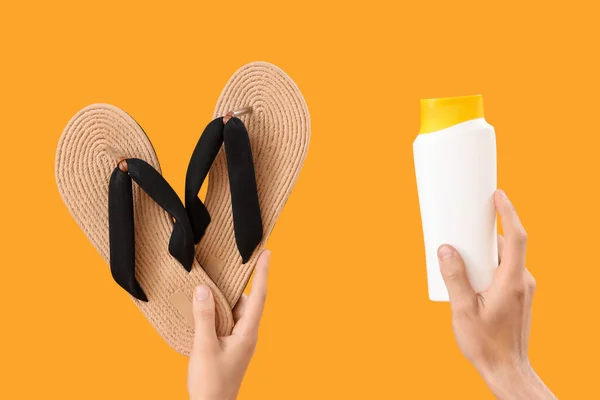 Female hands with bottle of sunscreen cream and flip flops on yellow background