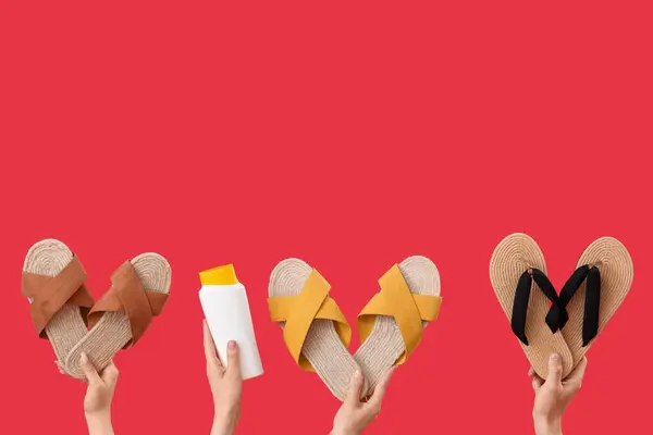 Female hands with bottle of sunscreen cream and flip flops on red background